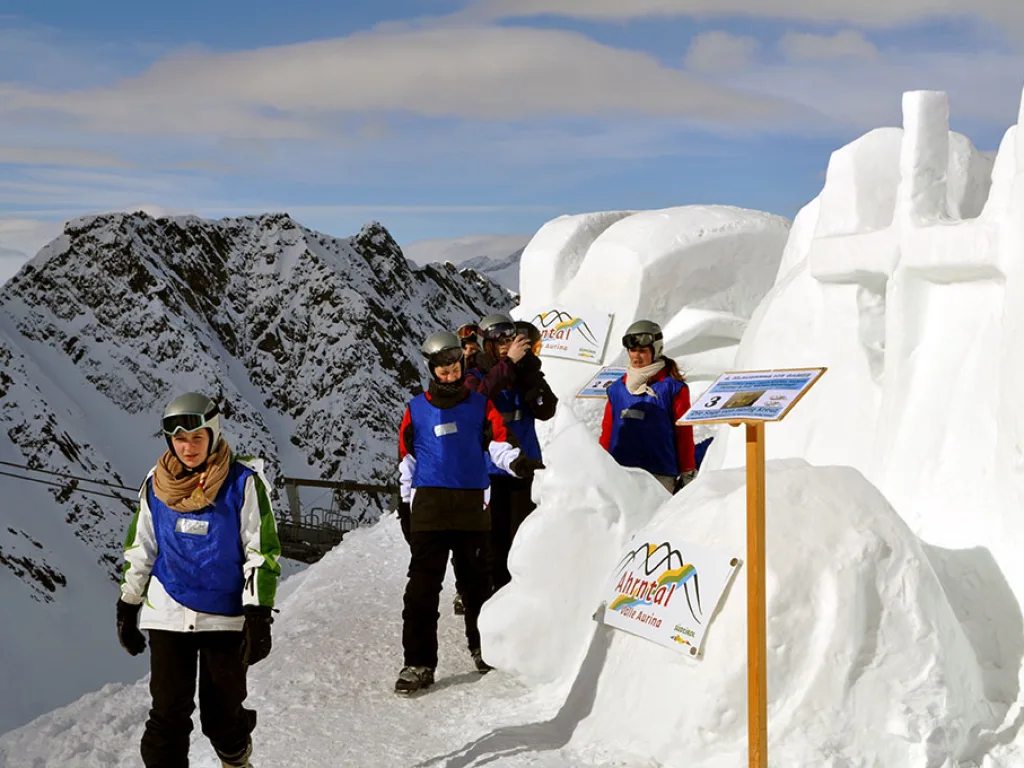 Jugendliche stehen vor einer Schneeskulptur an der Bergstation.